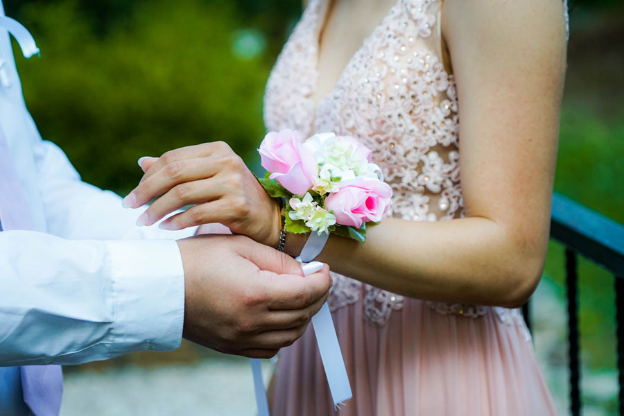 Image of a guy putting floral decor on girl's hand on prom night depicting the most important prom accessory girls might forget - prom night perfume `