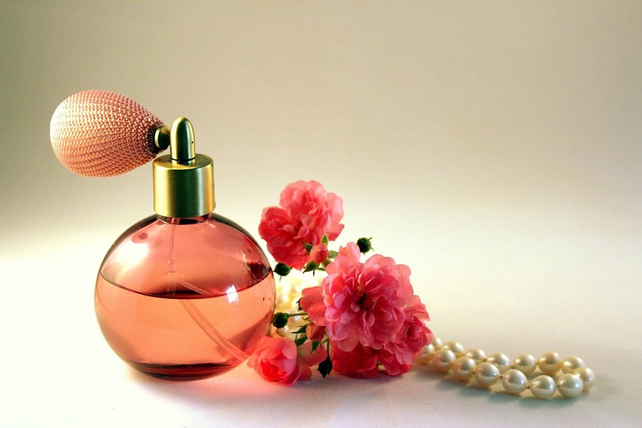 A bottle of perfume that has the rose fragrance with roses and beads next to it
