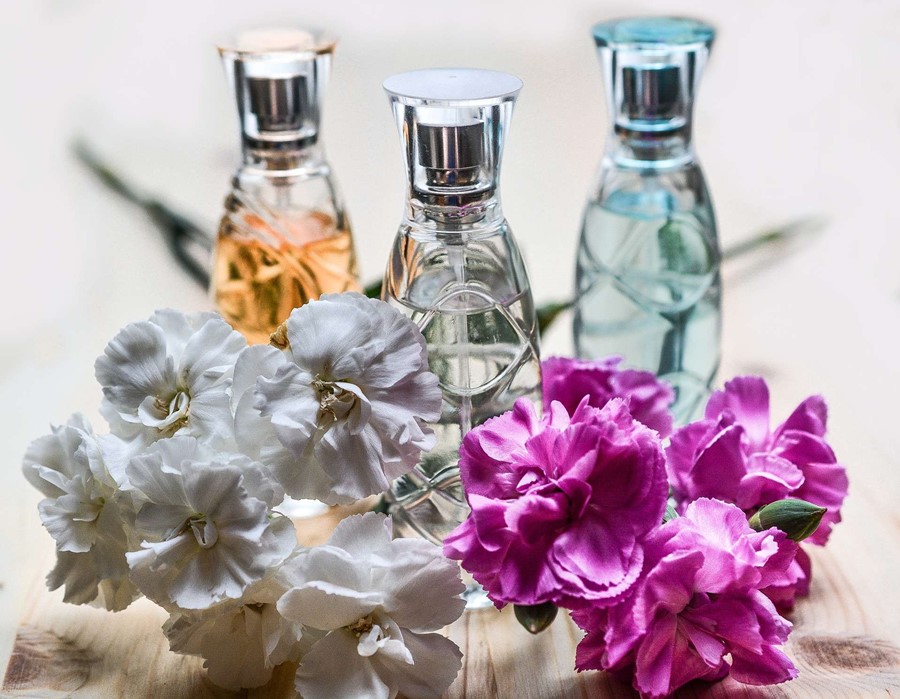 3 bottles of perfume that has 3 unique fragrances of flowers alongside some flowers