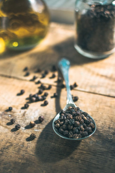 Image of a spoon full of black pepper with it's essential oil bottle from behind depicting the benefits of black pepper essential oil