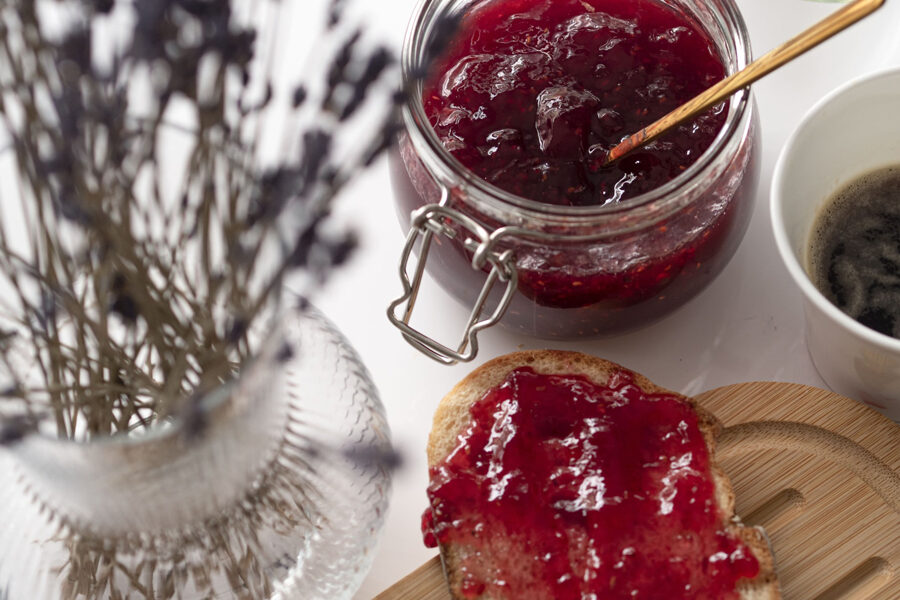 An image of a perfect moment captured - a jar of jam sitting pretty beside a slice of bread, lathered in the sweet spread.